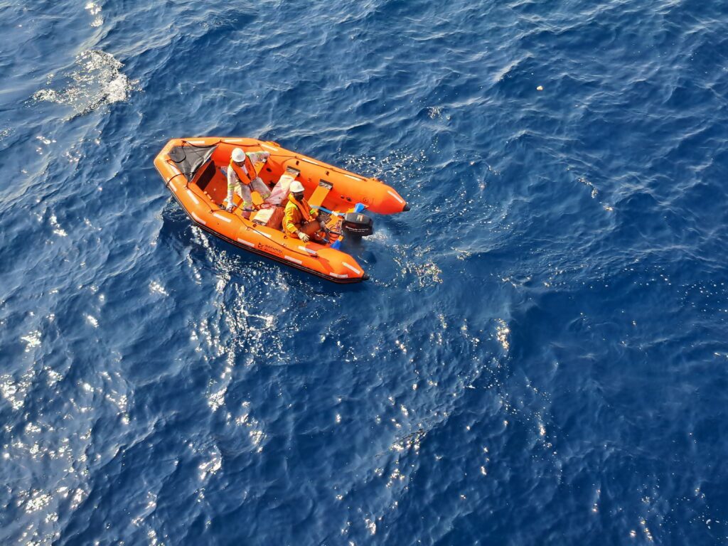 Aerial view of an orange inflatable boat navigating the open ocean with two people on board.